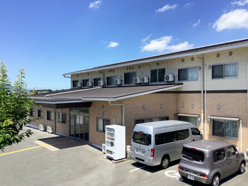 介護施設の建物外観。2階建てのレンガ造りで、駐車場に複数の車が停まっている